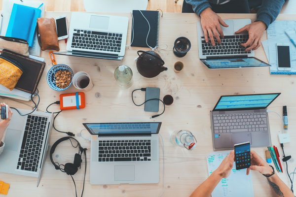 Stock image of multiple laptops on work table, several people's hands visible